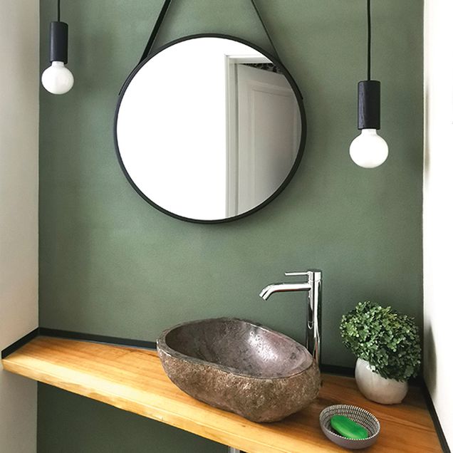 Waschtisch mit Holzfläche und Steinwaschbecken, oberhalb ein runder Spiegel und Glühbirnen